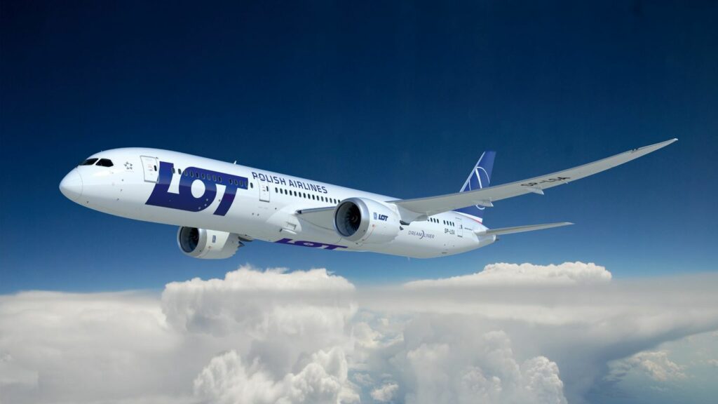 A LOT Polish Airlines Dreamliner airplane flies through a blue sky.
